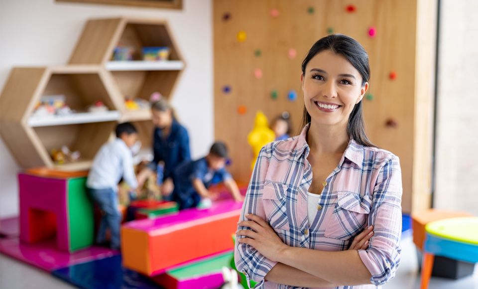 A woman standing, smiling with her arms crossed in a play room