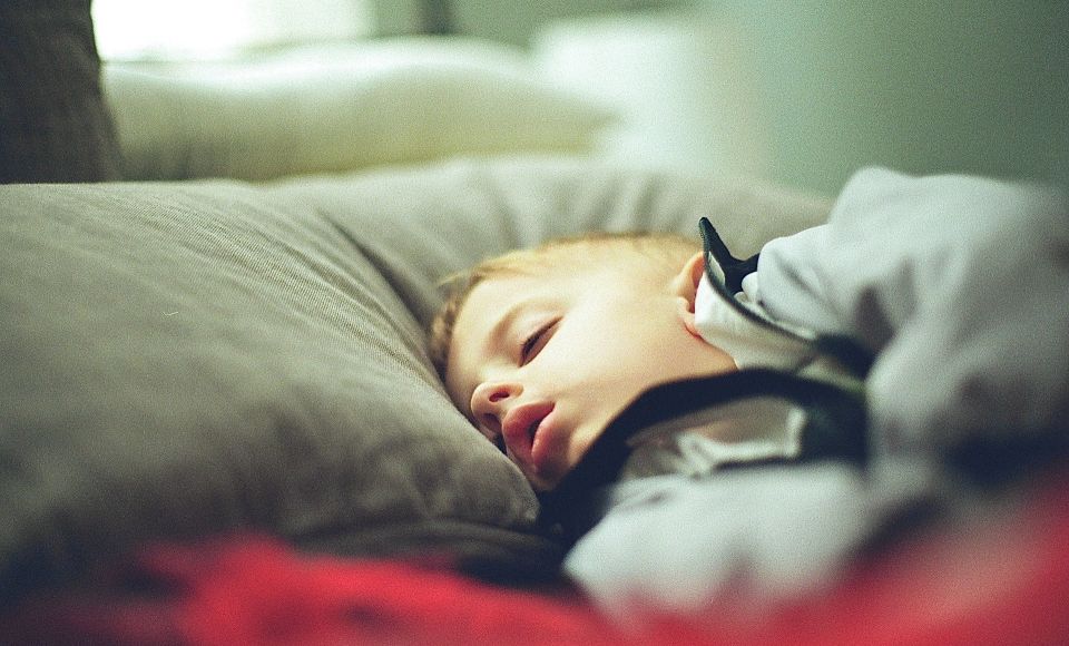 A young child sleeping on a bed with a red blanket